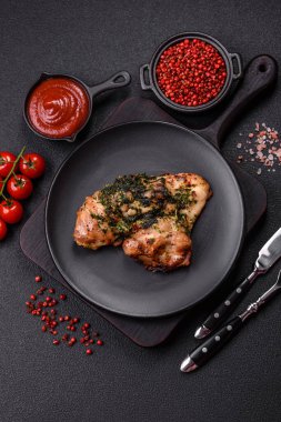 Koyu beton bir arka planda tuzlu, baharatlı ve otlu ızgara kemiksiz tavuk budu.