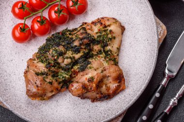 Koyu beton bir arka planda tuzlu, baharatlı ve otlu ızgara kemiksiz tavuk budu.