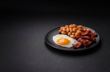 Yağda yumurta, pastırma, fasulye, domates, baharat ve bitkilerle İngiliz kahvaltısı. Güne doyurucu ve doyurucu bir başlangıç.