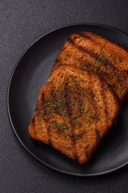 Lezzetli çıtır kıtır ekmek ya da esmer ekmekten yapılmış sarımsak soslu bruschetta ve koyu beton arka planda otlar.