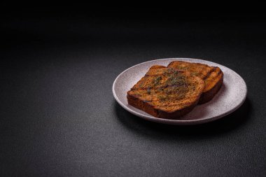 Lezzetli çıtır kıtır ekmek ya da esmer ekmekten yapılmış sarımsak soslu bruschetta ve koyu beton arka planda otlar.