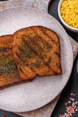 Lezzetli çıtır kıtır ekmek ya da esmer ekmekten yapılmış sarımsak soslu bruschetta ve koyu beton arka planda otlar.