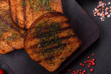 Lezzetli çıtır kıtır ekmek ya da esmer ekmekten yapılmış sarımsak soslu bruschetta ve koyu beton arka planda otlar.