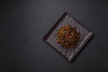 Koyu beton arka planda kırmızı biber, baharat ve tuz ile marine edilmiş lezzetli deniz yosunu. Lezzetli vejetaryen salatası