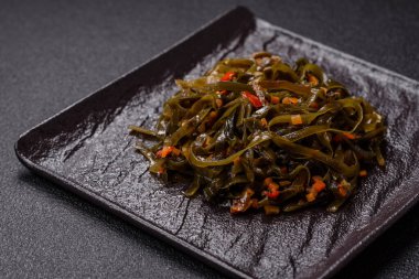 Koyu beton arka planda kırmızı biber, baharat ve tuz ile marine edilmiş lezzetli deniz yosunu. Lezzetli vejetaryen salatası