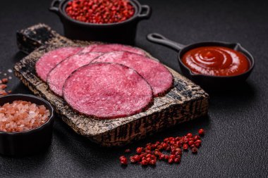 Lezzetli füme salam. Tuz, baharat ve otlarla dilimlenmiş. Koyu beton bir arka planda.