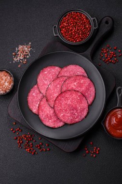 Lezzetli füme salam. Tuz, baharat ve otlarla dilimlenmiş. Koyu beton bir arka planda.