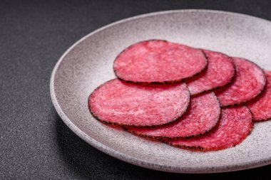 Lezzetli füme salam. Tuz, baharat ve otlarla dilimlenmiş. Koyu beton bir arka planda.