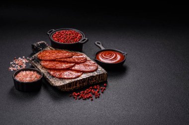 Lezzetli tütsülenmiş sucuklu sosis. Tuz, baharat ve otlarla dilimlenmiş. Koyu beton arka planda.