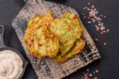 Sarımsaklı, tuzlu, baharatlı sebzeli kabaklı börek ve koyu beton arka planda beyaz soslu otlar.