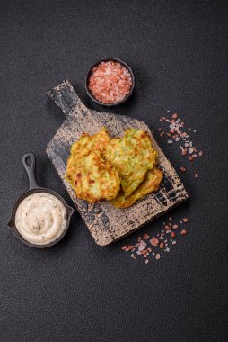 Sarımsaklı, tuzlu, baharatlı sebzeli kabaklı börek ve koyu beton arka planda beyaz soslu otlar.