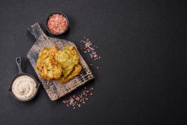 Sarımsaklı, tuzlu, baharatlı sebzeli kabaklı börek ve koyu beton arka planda beyaz soslu otlar.