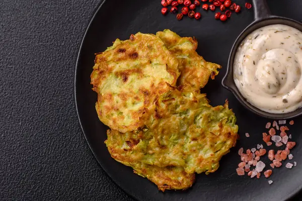 Sarımsaklı, tuzlu, baharatlı sebzeli kabaklı börek ve koyu beton arka planda beyaz soslu otlar.