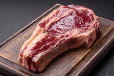 Taze, çiğ biftek, tuz, baharat ve otlar koyu dokulu arka planda.