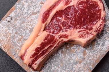 Taze, çiğ biftek, tuz, baharat ve otlar koyu dokulu arka planda.