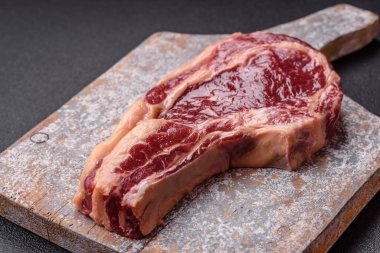 Taze, çiğ biftek, tuz, baharat ve otlar koyu dokulu arka planda.