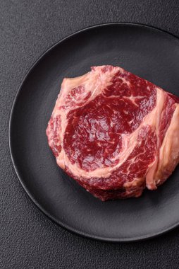 Taze, çiğ biftek, tuz, baharat ve otlar koyu dokulu arka planda.