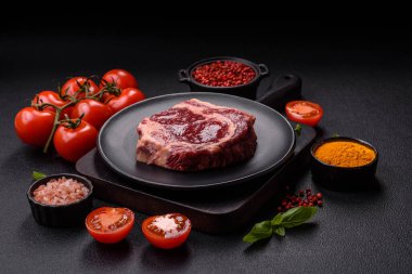 Taze, çiğ biftek, tuz, baharat ve otlar koyu dokulu arka planda.