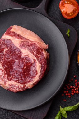 Taze, çiğ biftek, tuz, baharat ve otlar koyu dokulu arka planda.