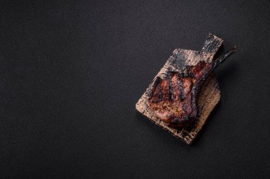 Koyu beton arka planda tuzlu, baharatlı ve otlu sulu ızgara baltalı biftek.