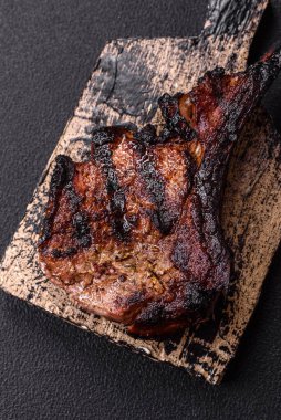 Koyu beton arka planda tuzlu, baharatlı ve otlu sulu ızgara baltalı biftek.