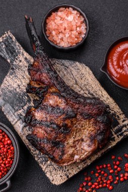 Koyu beton arka planda tuzlu, baharatlı ve otlu sulu ızgara baltalı biftek.