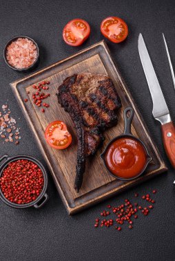 Koyu beton arka planda tuzlu, baharatlı ve otlu sulu ızgara baltalı biftek.