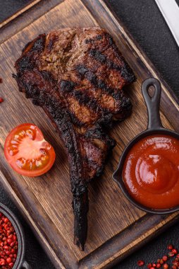 Koyu beton arka planda tuzlu, baharatlı ve otlu sulu ızgara baltalı biftek.