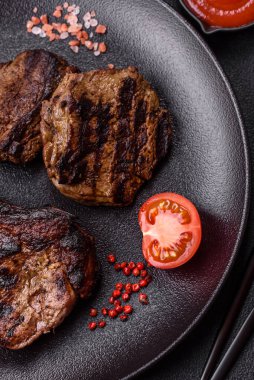 Koyu beton arka planda tuzlu, baharatlı ve otlu sulu ızgara baltalı biftek.