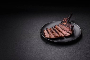 Koyu beton arka planda tuzlu, baharatlı ve otlu sulu ızgara baltalı biftek.