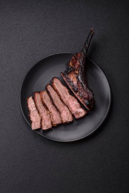 Koyu beton arka planda tuzlu, baharatlı ve otlu sulu ızgara baltalı biftek.