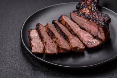 Koyu beton arka planda tuzlu, baharatlı ve otlu sulu ızgara baltalı biftek.