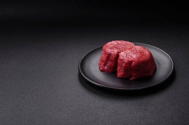 Koyu beton arka planda tuz ve baharatlı taze çiğ et madalyonları.