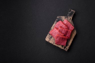 Tuz, baharat ve otlarla sulu taze çiğ et, koyu dokulu beton arka planda.