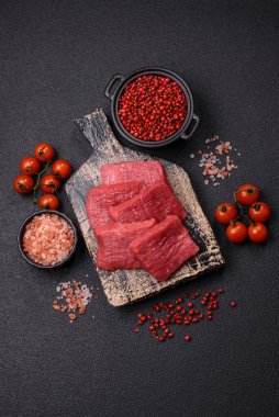 Tuz, baharat ve otlarla sulu taze çiğ et, koyu dokulu beton arka planda.