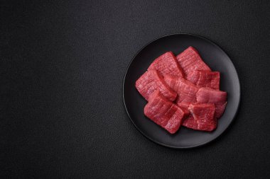 Tuz, baharat ve otlarla sulu taze çiğ et, koyu dokulu beton arka planda.