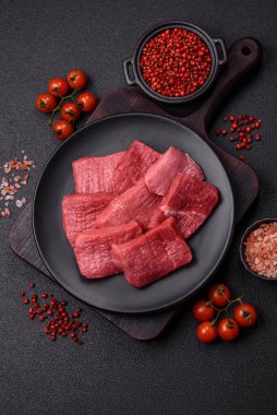 Tuz, baharat ve otlarla sulu taze çiğ et, koyu dokulu beton arka planda.