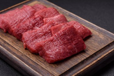 Tuz, baharat ve otlarla sulu taze çiğ et, koyu dokulu beton arka planda.