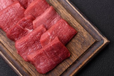 Tuz, baharat ve otlarla sulu taze çiğ et, koyu dokulu beton arka planda.