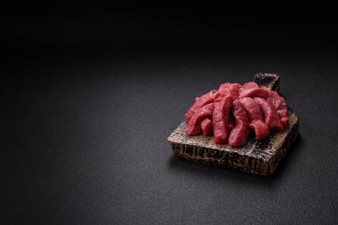 Tuz, baharat ve otlarla sulu taze çiğ et, koyu dokulu beton arka planda.