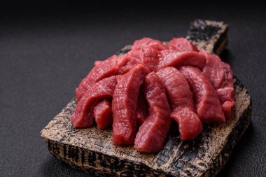 Tuz, baharat ve otlarla sulu taze çiğ et, koyu dokulu beton arka planda.