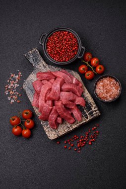 Tuz, baharat ve otlarla sulu taze çiğ et, koyu dokulu beton arka planda.