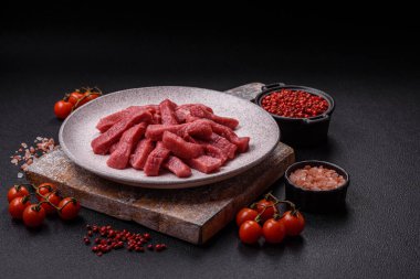 Tuz, baharat ve otlarla sulu taze çiğ et, koyu dokulu beton arka planda.