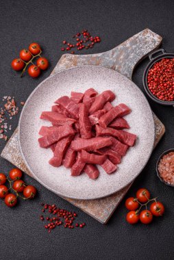 Tuz, baharat ve otlarla sulu taze çiğ et, koyu dokulu beton arka planda.