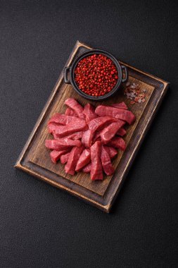 Tuz, baharat ve otlarla sulu taze çiğ et, koyu dokulu beton arka planda.