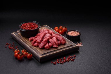 Tuz, baharat ve otlarla sulu taze çiğ et, koyu dokulu beton arka planda.