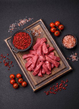 Tuz, baharat ve otlarla sulu taze çiğ et, koyu dokulu beton arka planda.