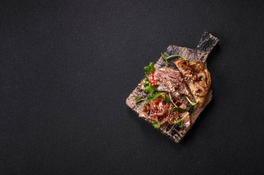 Koyu beton bir zemin üzerinde jambon, mantar ve dana eti, domates ve mikroçerez içeren çeşitli tostlar veya bruschetta çeşitleri