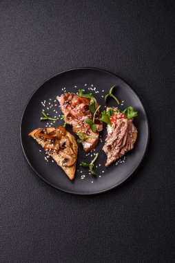 Koyu beton bir zemin üzerinde jambon, mantar ve dana eti, domates ve mikroçerez içeren çeşitli tostlar veya bruschetta çeşitleri