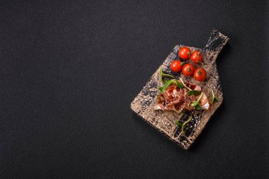 Koyu beton bir zemin üzerinde jambon, mantar ve dana eti, domates ve mikroçerez içeren çeşitli tostlar veya bruschetta çeşitleri
